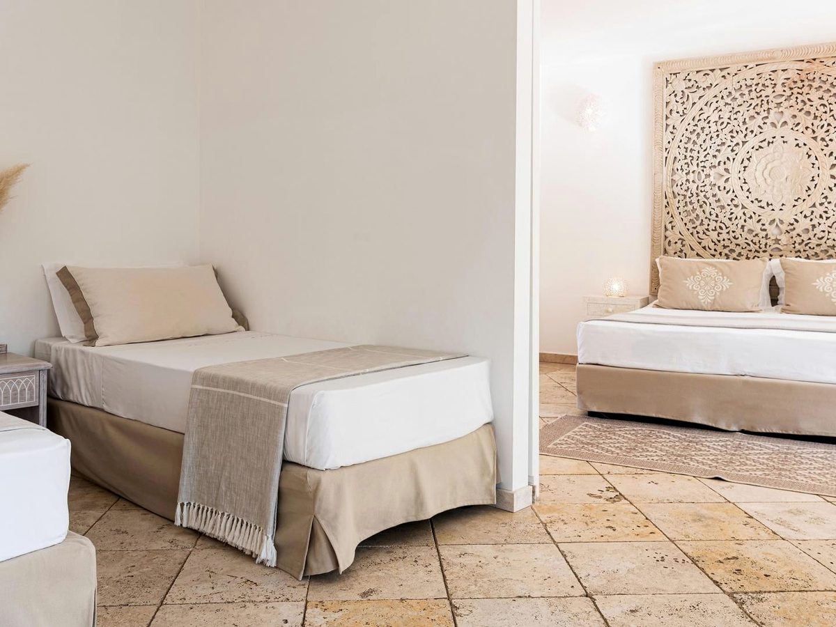Two single beds with woven throws and a carved headboard in a room with a tiled floor and neutral tones.