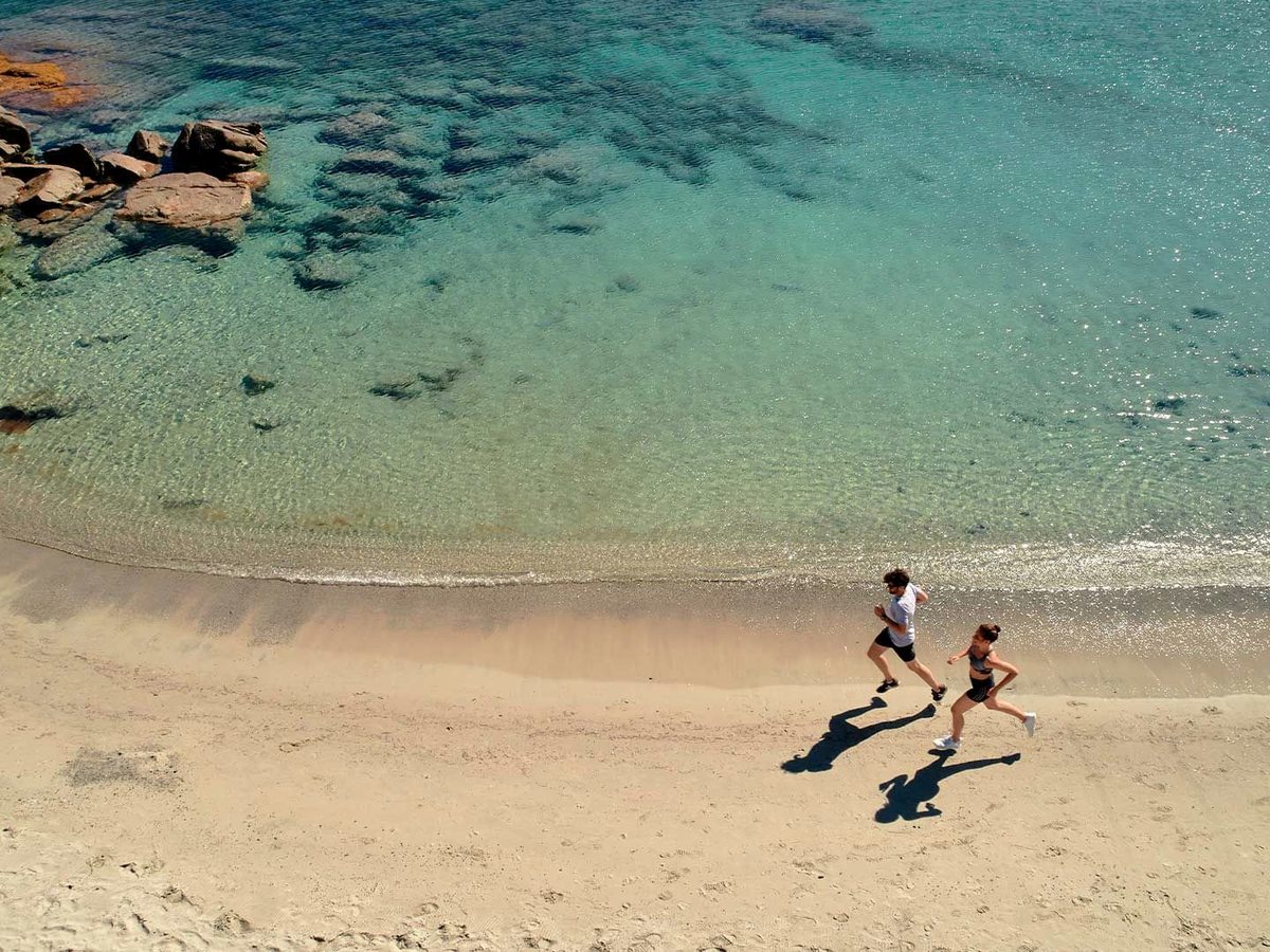 Two people jogging along the wet sand at the edge of clear, shallow turquoise water.