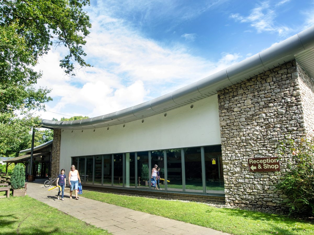 The curved zinc-roofed reception and shop building in local limestone, with a paved path across the lawn.