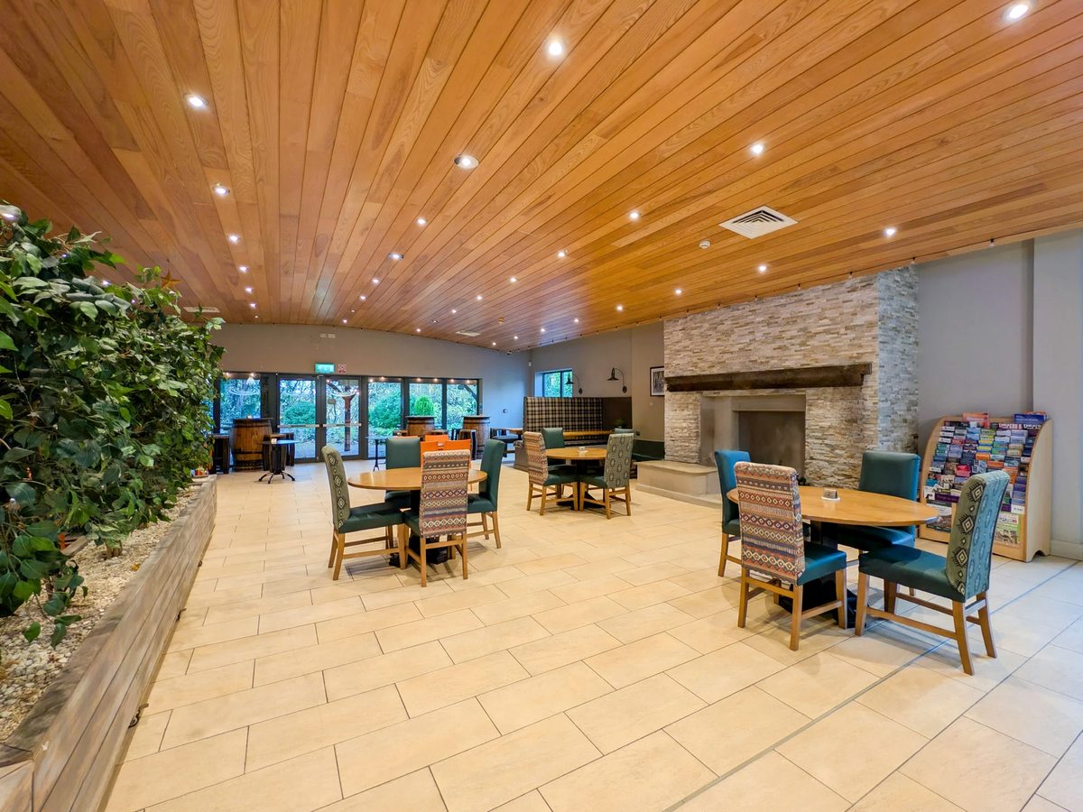 The Woodland Edge dining room with a fireplace, cushioned chairs and a timber-panelled ceiling.