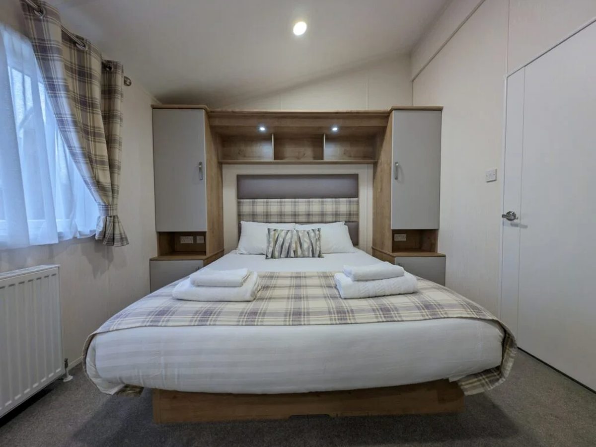 A made-up double bed with a tartan throw, fitted wardrobes and a side window.
