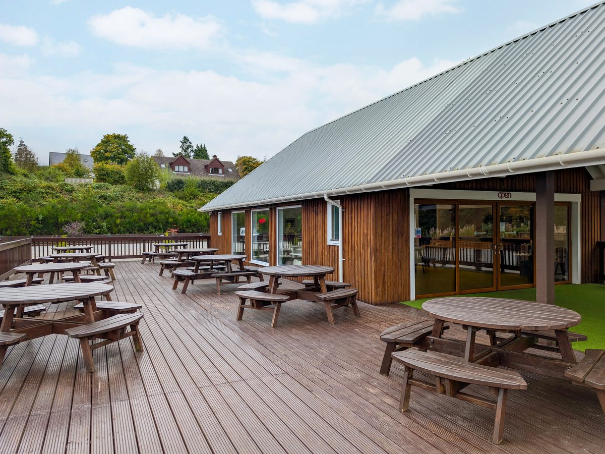 The Woodland Edge decked terrace with round picnic tables beside the timber-clad restaurant.