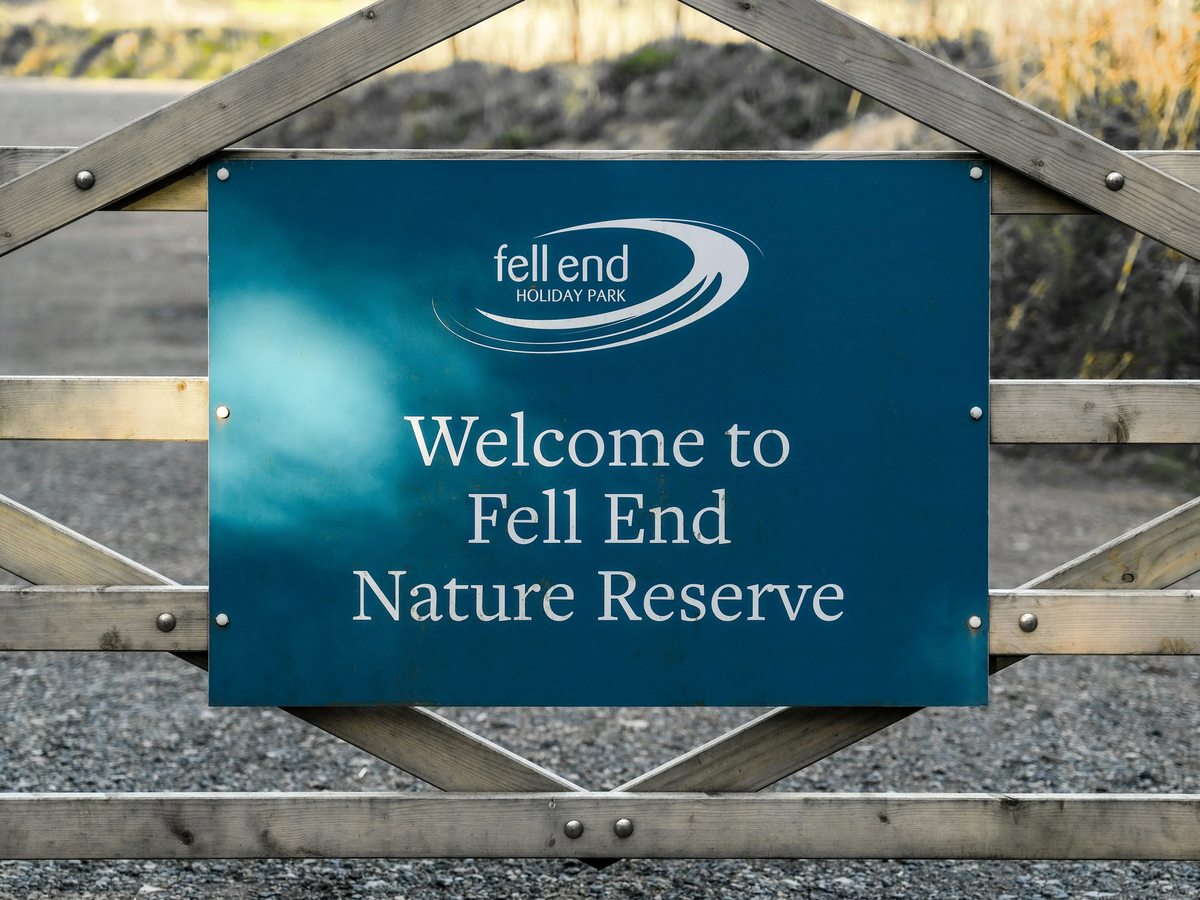 A blue Fell End Holiday Park sign reading Welcome to Fell End Nature Reserve, fixed to a wooden gate.