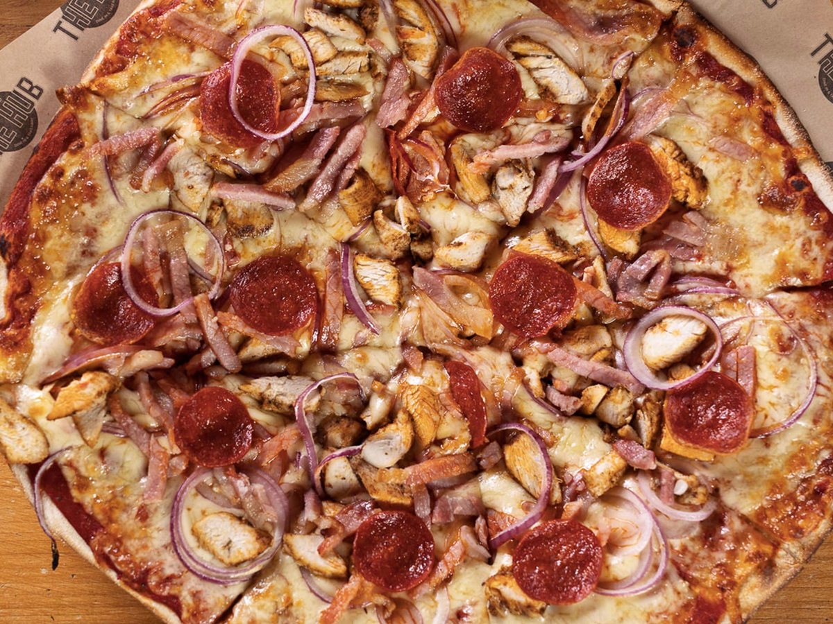 A thin-crust pizza topped with pepperoni, chicken, ham and red onion on branded paper