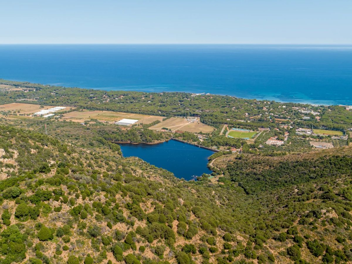 Aerial view of woodland, farm fields, an inland lake and the Sardinian coastline under a clear sky