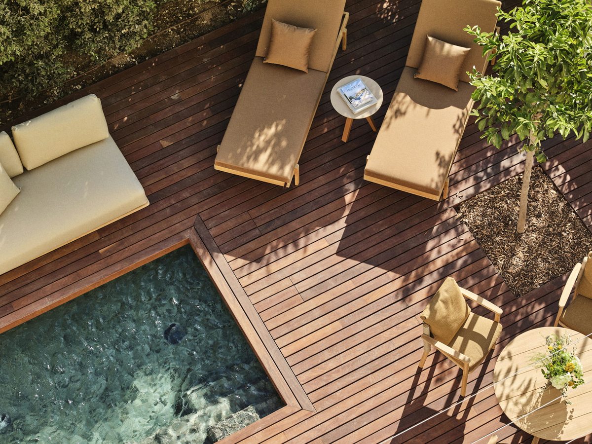 Overhead view of a timber deck with a plunge pool, cushioned loungers, a daybed sofa and a potted tree.