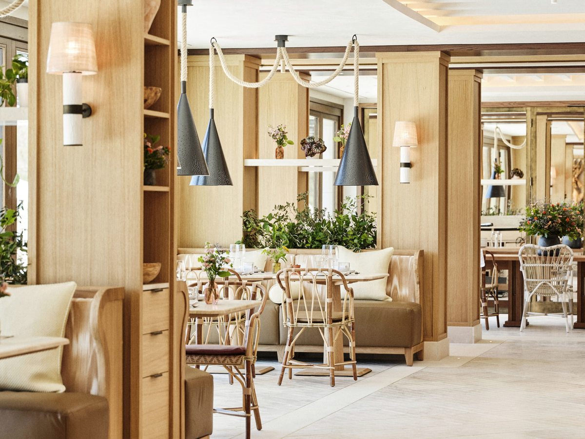 The interior of Mel, with pale timber panelling, rattan bistro chairs, cushioned banquettes and black conical pendant lights.