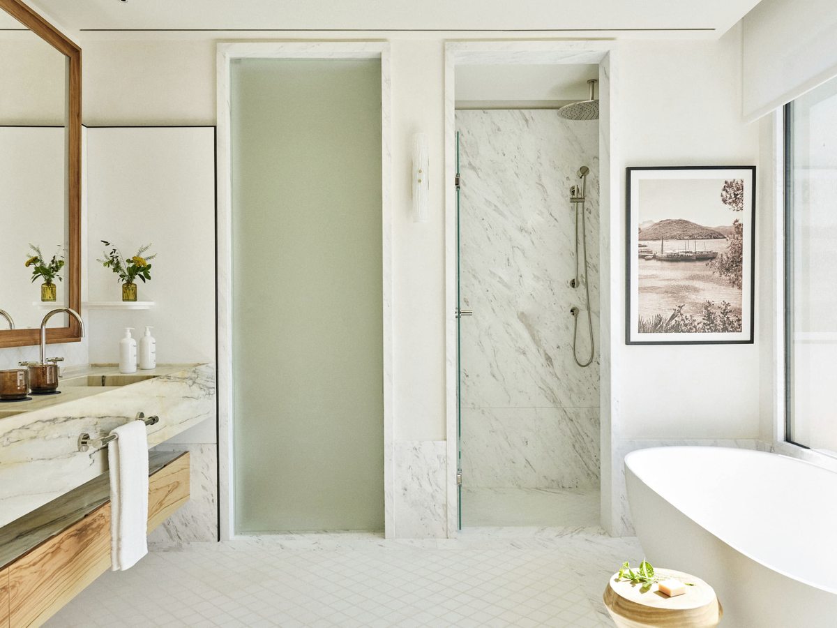 A marble bathroom with a twin vanity, a walk-in rainfall shower and a freestanding bathtub by the window.