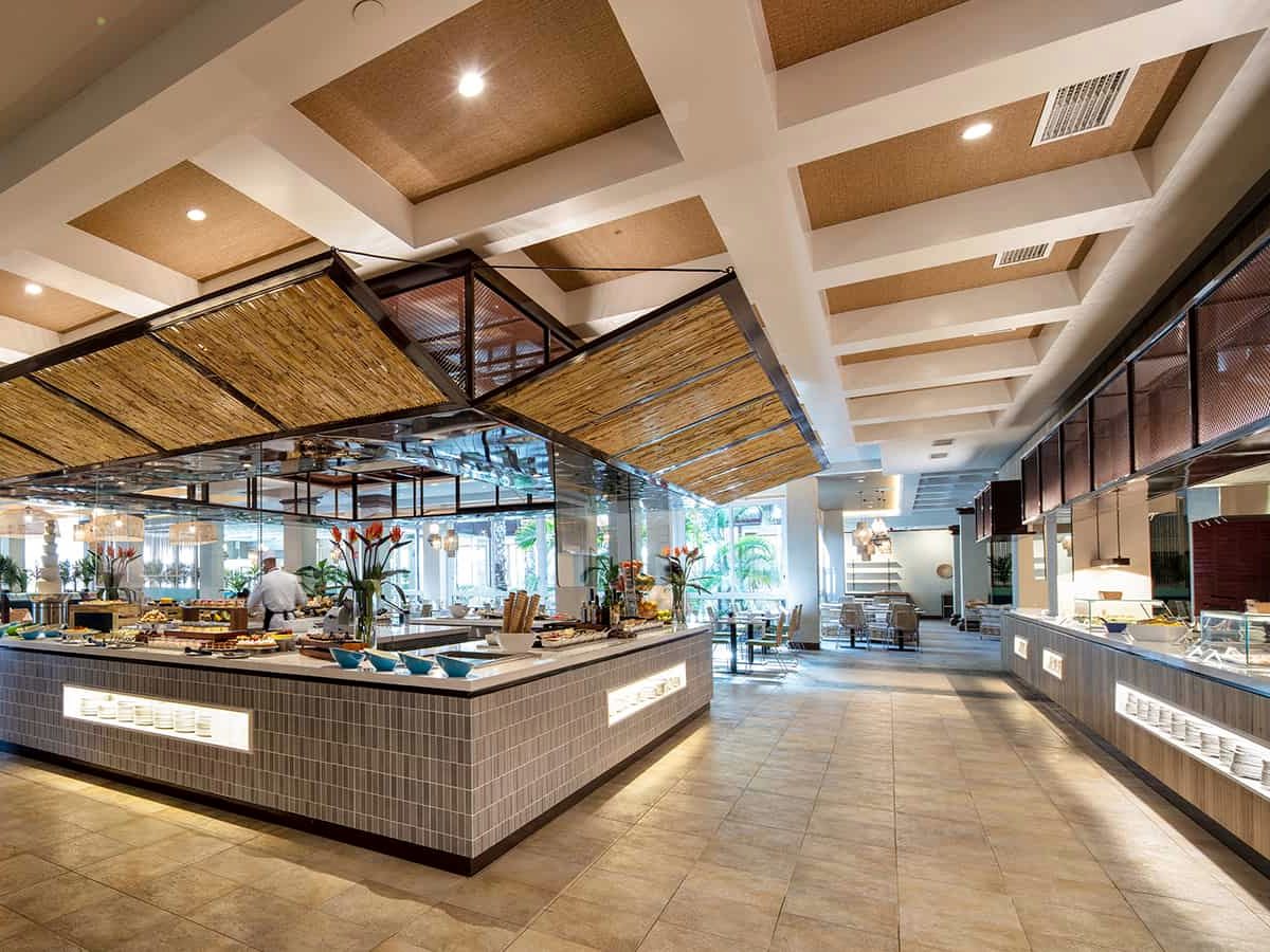 A buffet counter with a live cooking station under a high white-beamed ceiling, staff serving behind it.