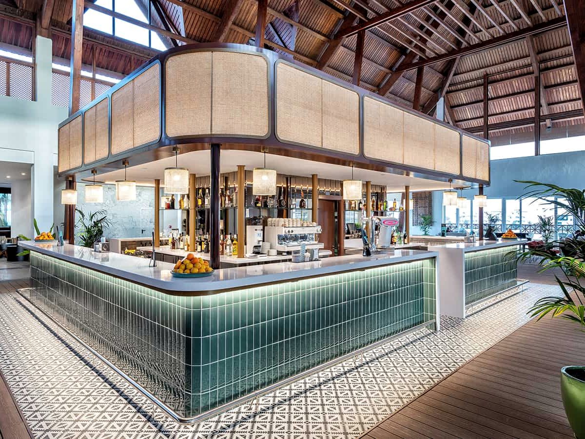 A curved bar counter faced in green tiles under a tall timber-and-cane canopy, stools around it.