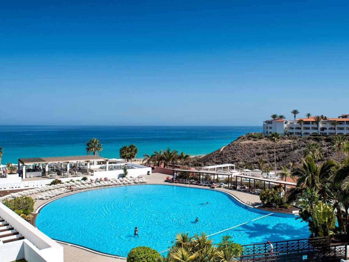 A pool on a terrace above the coast, loungers around it and the sea and cliffs behind.
