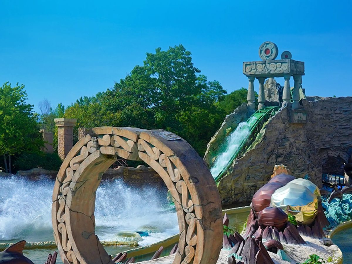 A splash boat ride at Gardaland Park with a large wooden wheel feature and rockwork, water spraying up around the channel.