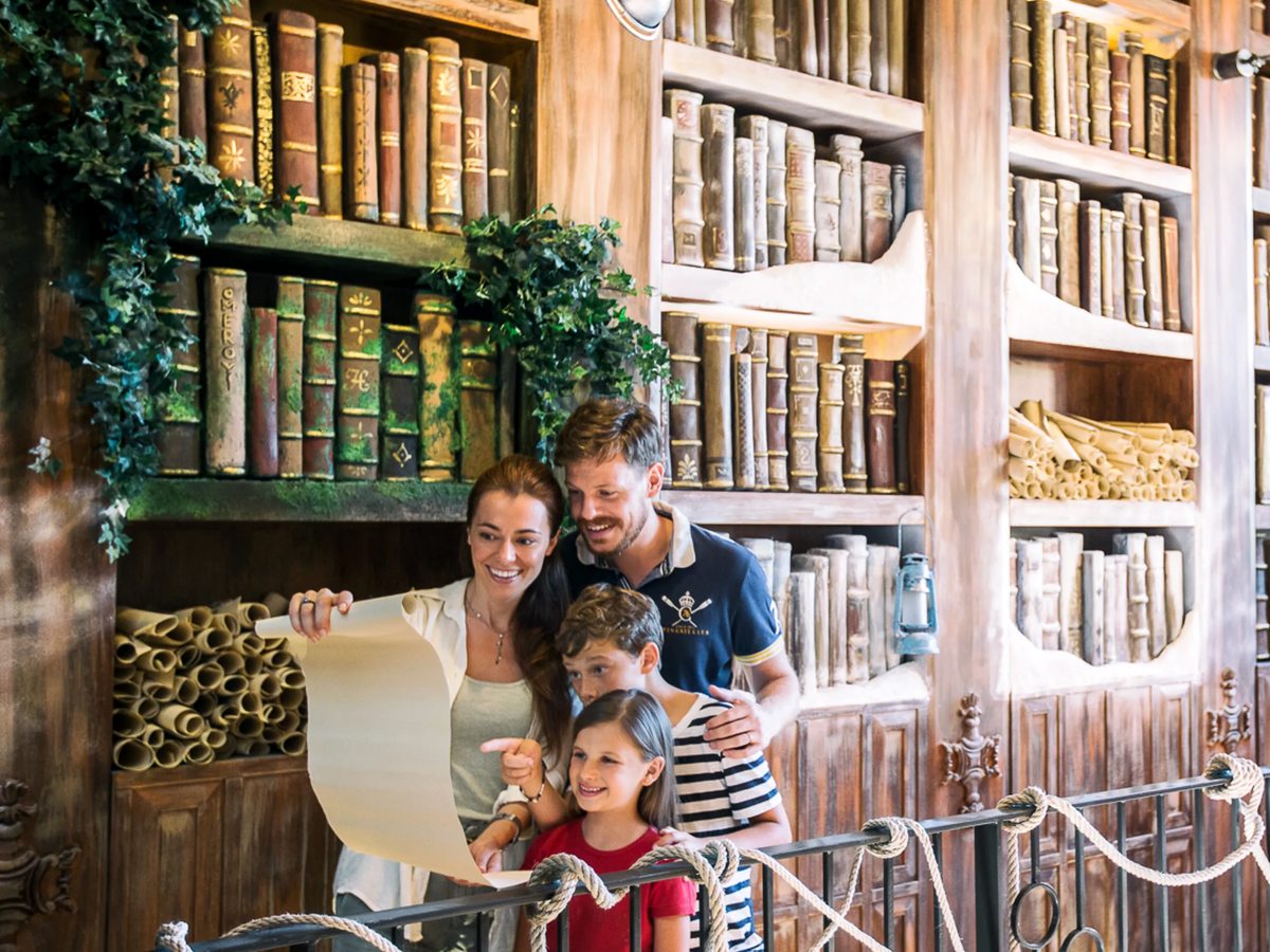An indoor corner made up as an old library, with faux bookcases, scroll props and ivy, roped off as a photo spot for families.