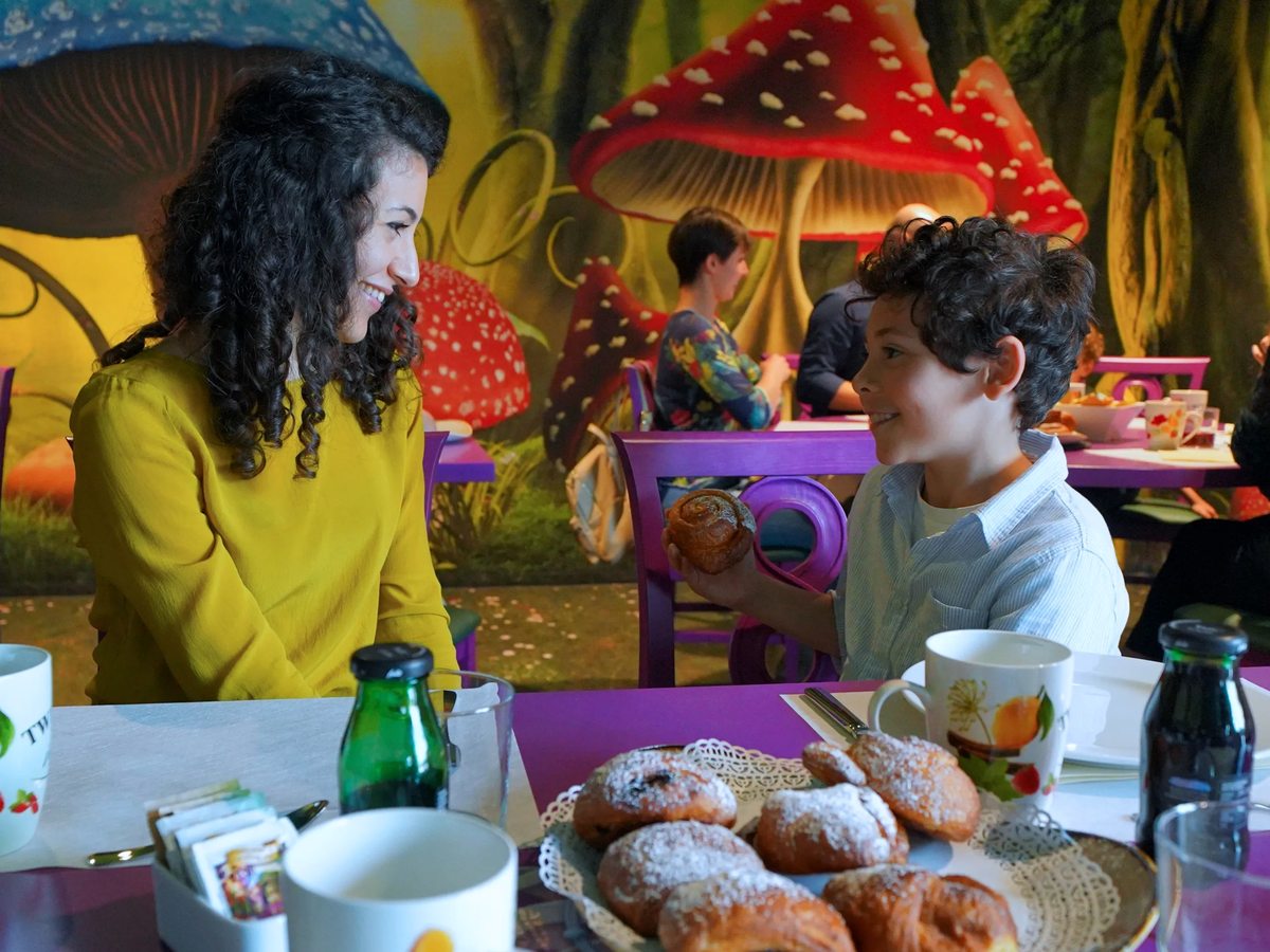 A breakfast spread of pastries and mugs on purple tables in the woodland-themed Quercia Magica, among oversized toadstool decorations.