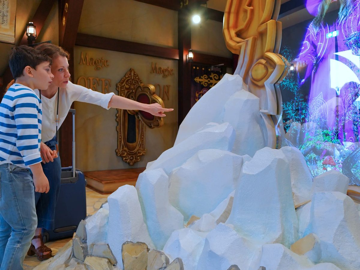 A themed hotel lobby with a glowing white ice-effect sculpture, where a child and an adult stop to look at it.