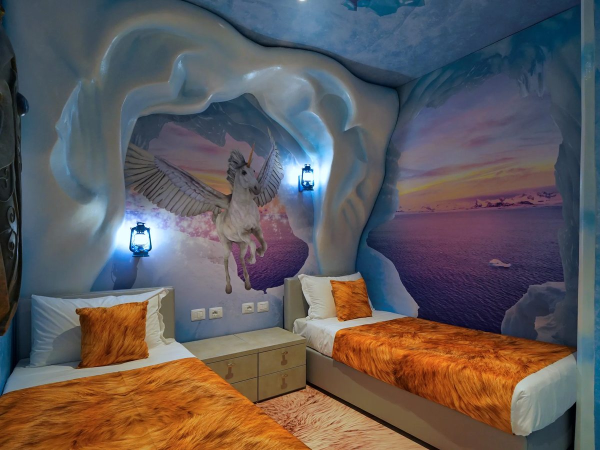 Two single beds beneath a unicorn mural and a sculpted ice-effect headboard in a Magic Ice Castle themed room.
