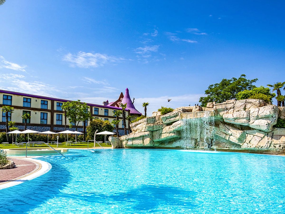 The large Blue Lagoon outdoor pool with a central rock feature, white parasols on the sun terrace and resort buildings behind.