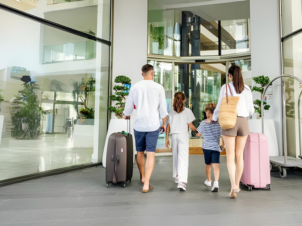 A family with wheeled suitcases walking into GF Victoria's bright, glass-fronted lobby entrance.