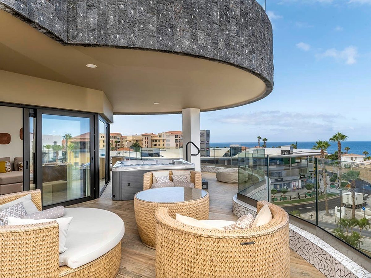 A sea-view terrace with a private hot tub and round woven tub chairs under a curved cast stone canopy.