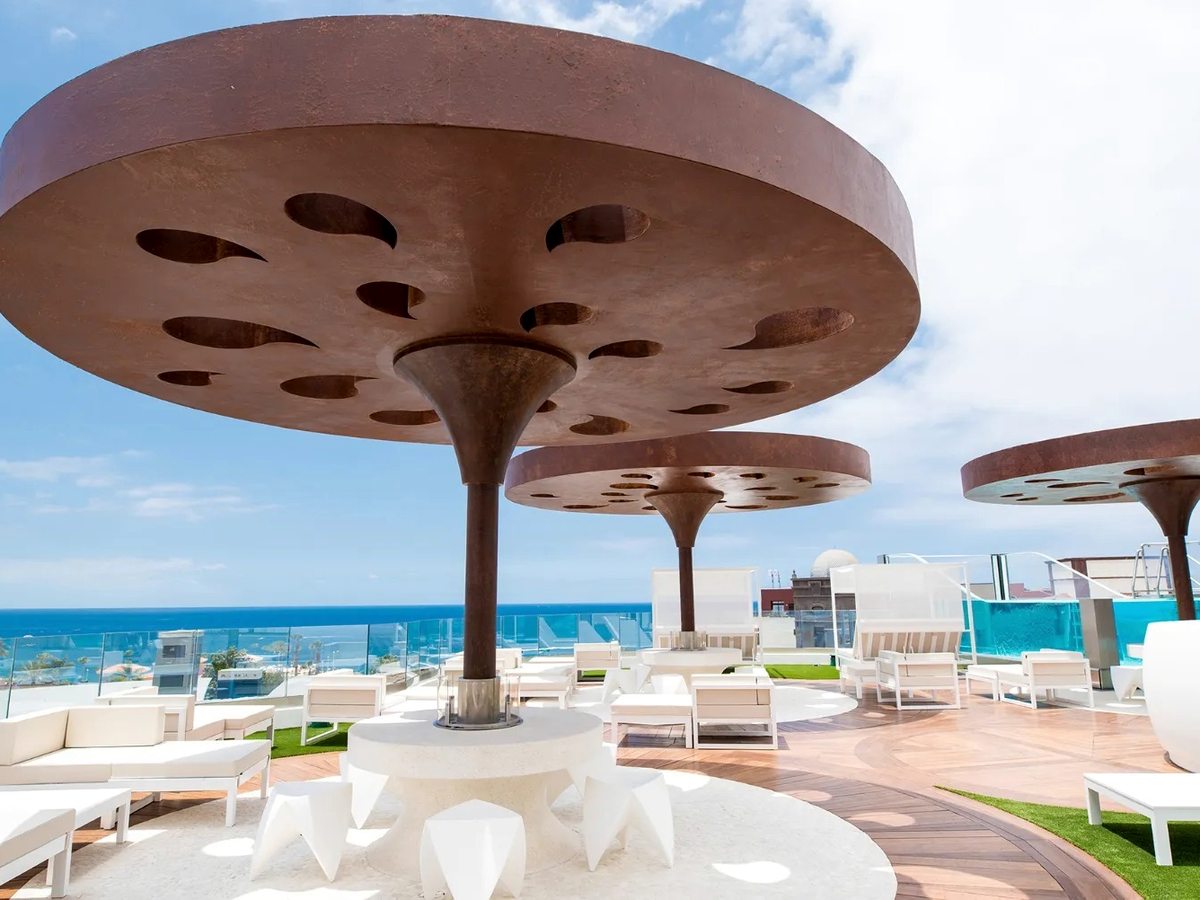 A rooftop terrace with sculptural rust-coloured mushroom canopies, white daybeds and open sea views.