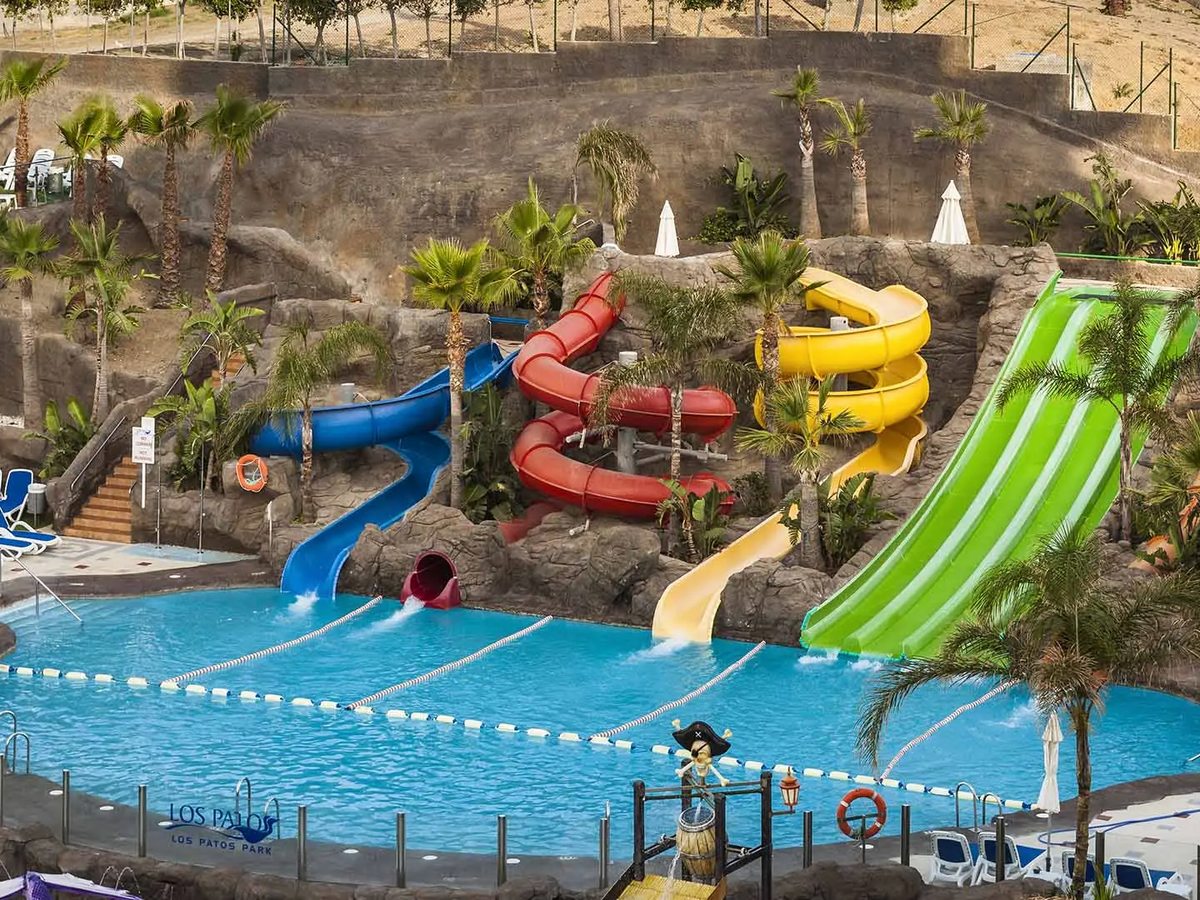 Red, green and yellow tube water slides winding down a rocky slope into a splash pool.