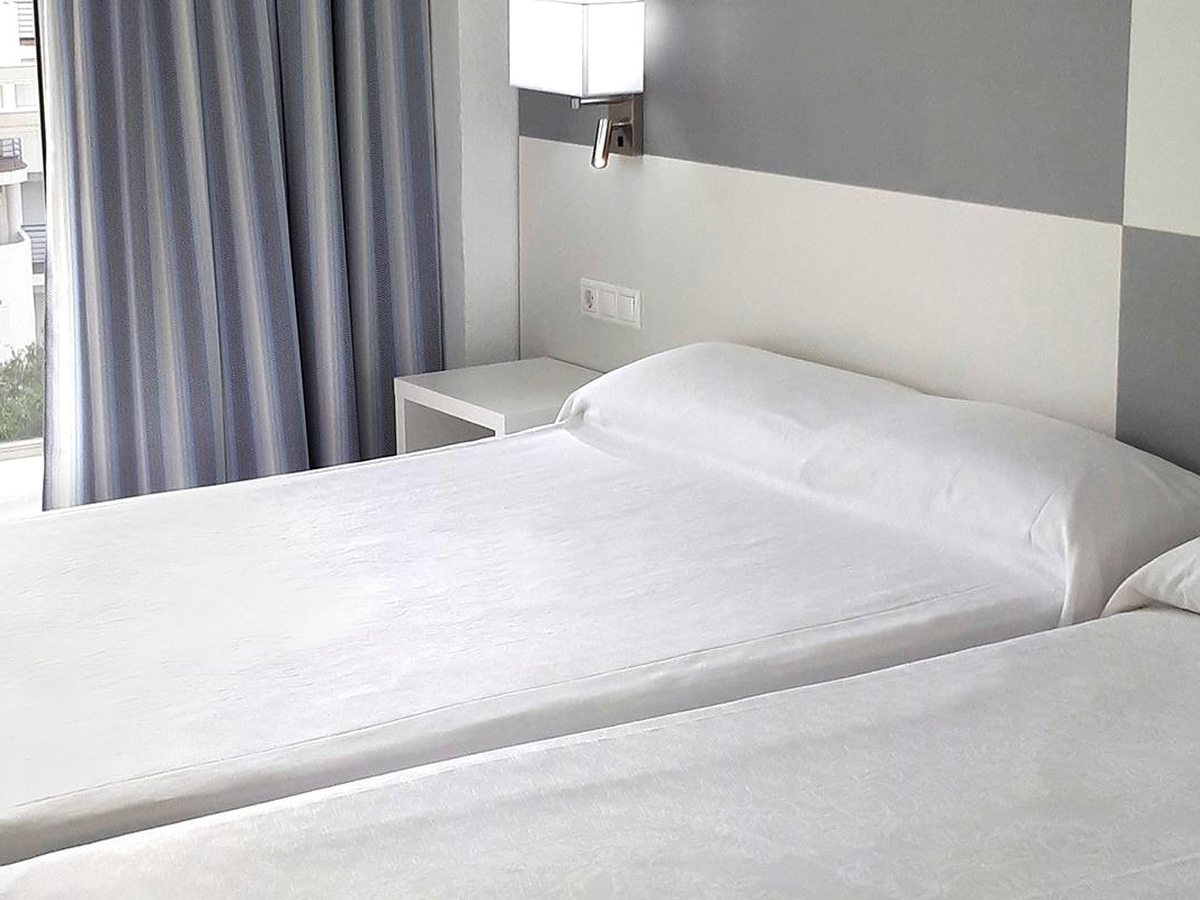 A twin room with two single beds under white bedding, a grey headboard and a curtained window.
