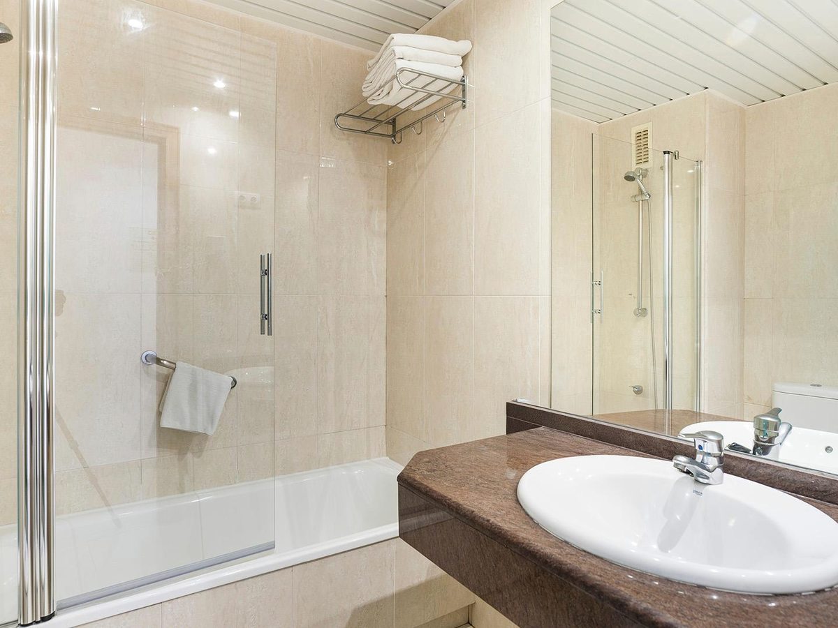 A bathroom with a glass shower screen over a bath, a sink on a dark countertop and a large mirror.