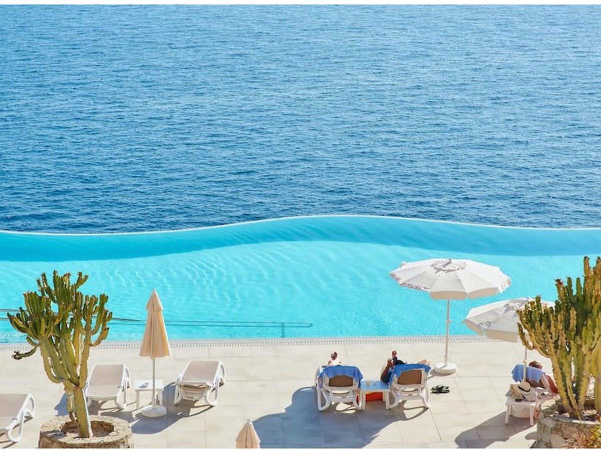 Clifftop pool terrace with sun loungers, white parasols and cactus planters overlooking the sea.