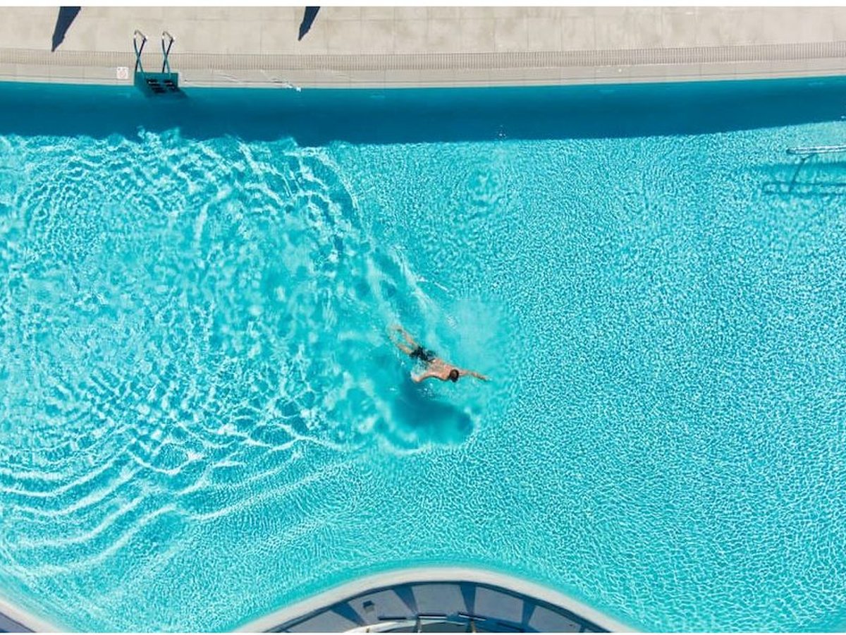 Overhead view of a large freeform swimming pool with one person swimming across the turquoise water.