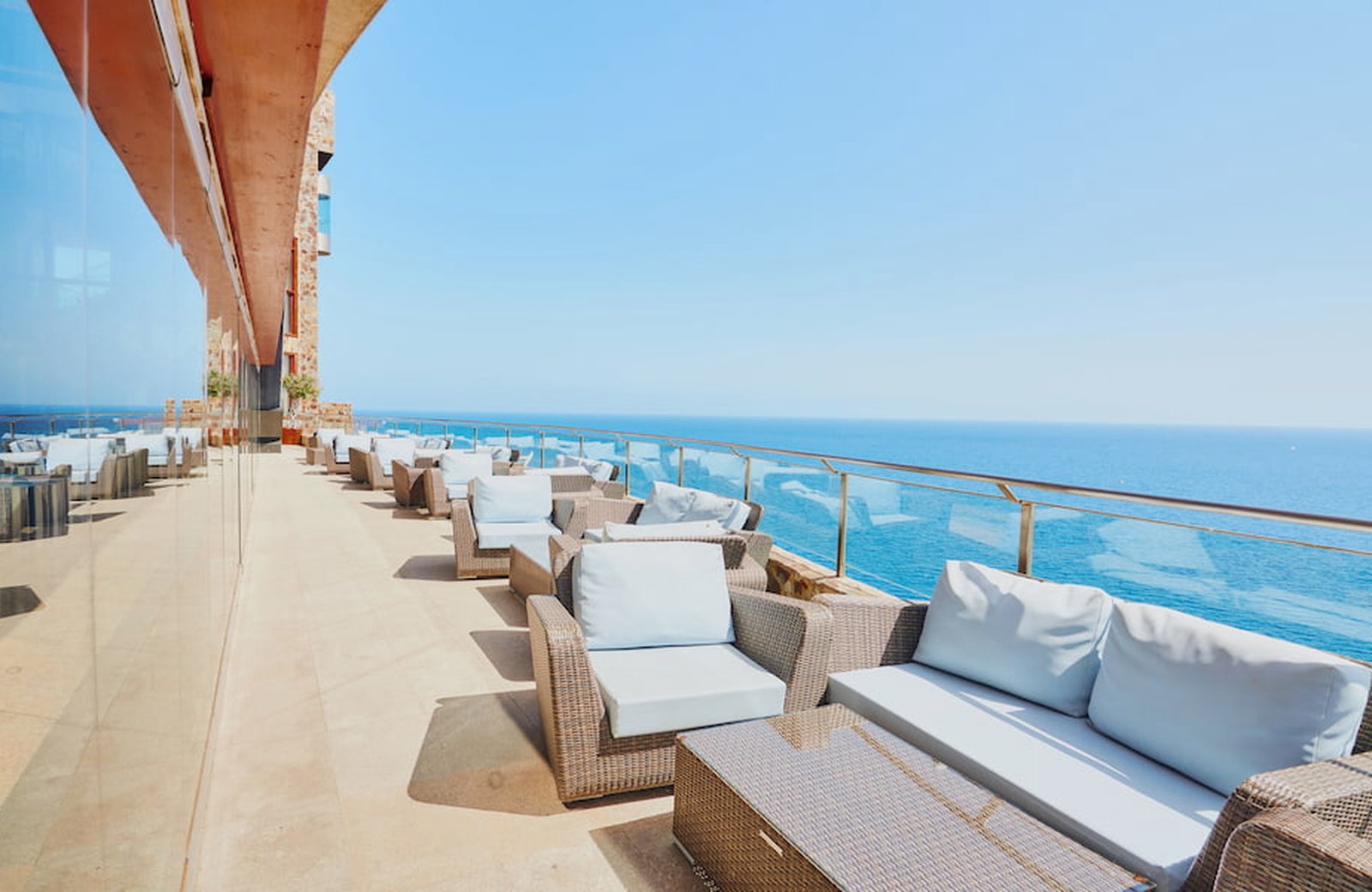 Terrace of wicker sofas and low tables at Gloria Palace Amadores, the Atlantic beyond the glass rail