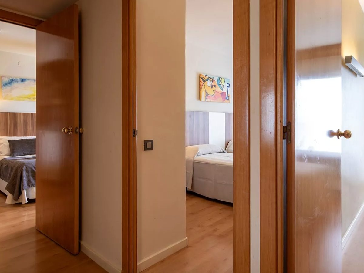 An internal hallway with wooden doors opening to two separate bedrooms, one with a double bed and one with a single, and a cartoon picture on the wall.