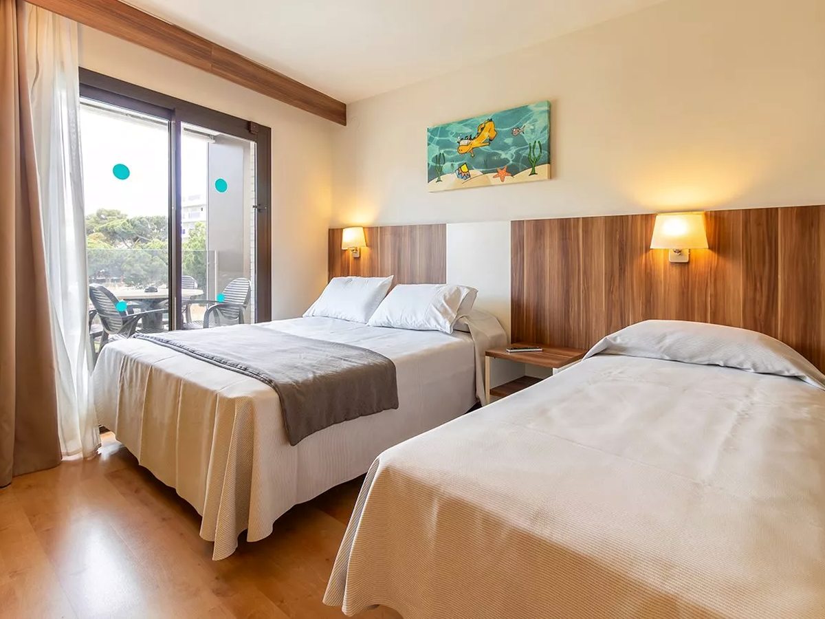 A bedroom with a double and a single bed, wooden headboards, a fish mural above, and a sliding glass door onto a furnished balcony.