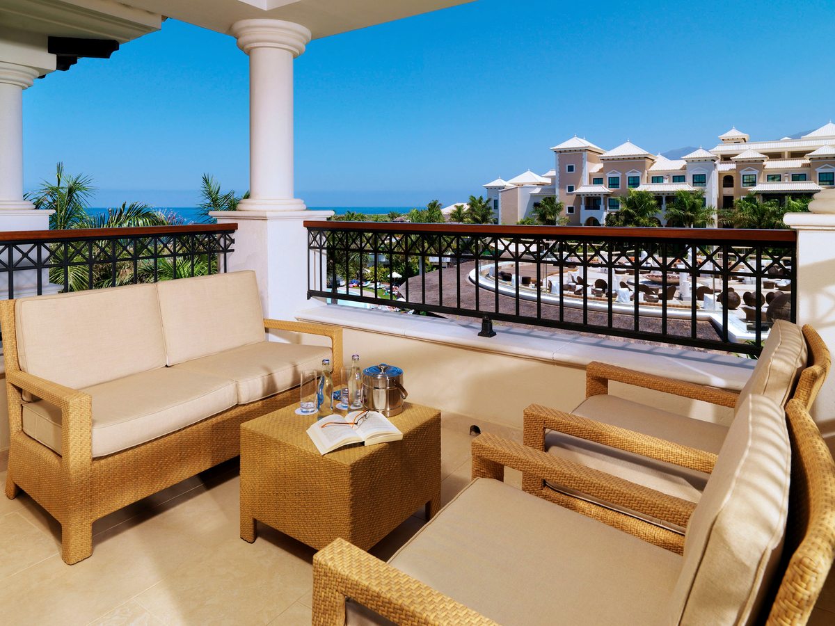 A covered balcony with wicker sofas and armchairs, columns and a railing, the resort and sea beyond.