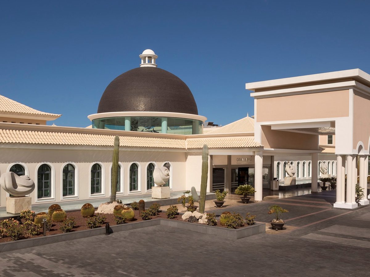 The cream-tiled entrance building topped by a black-tiled dome, with a cactus and succulent garden and sculptures out front.
