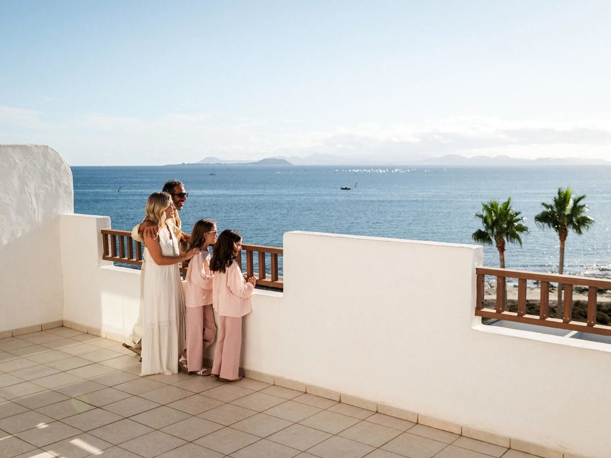 A family at the railing of a tiled private terrace looking out over the Atlantic, with palms along a low wall.