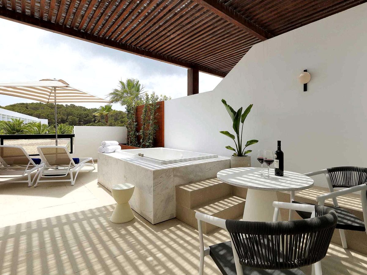 Private suite terrace with a sunken outdoor hot tub, sun loungers, a parasol and a dining set on striped decking.