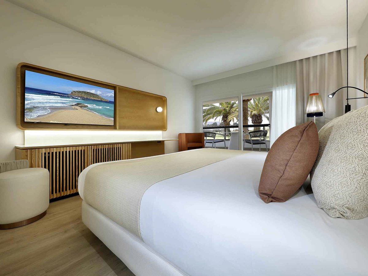 Double room with a king bed and white bedding, a wall-mounted TV on a wood-slatted panel and bedside reading lights.