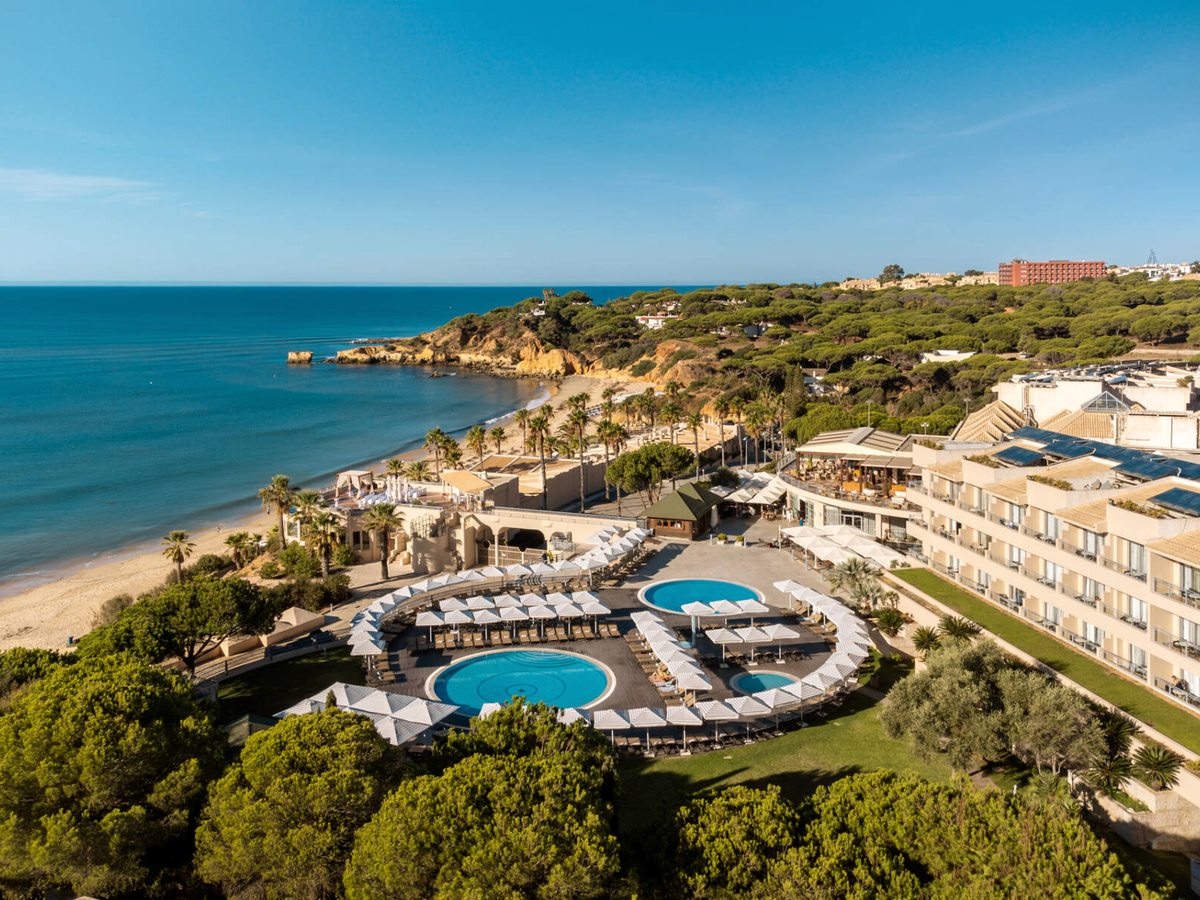 An aerial view of the clifftop resort, its pools and gardens, above the sandy cove and sea.