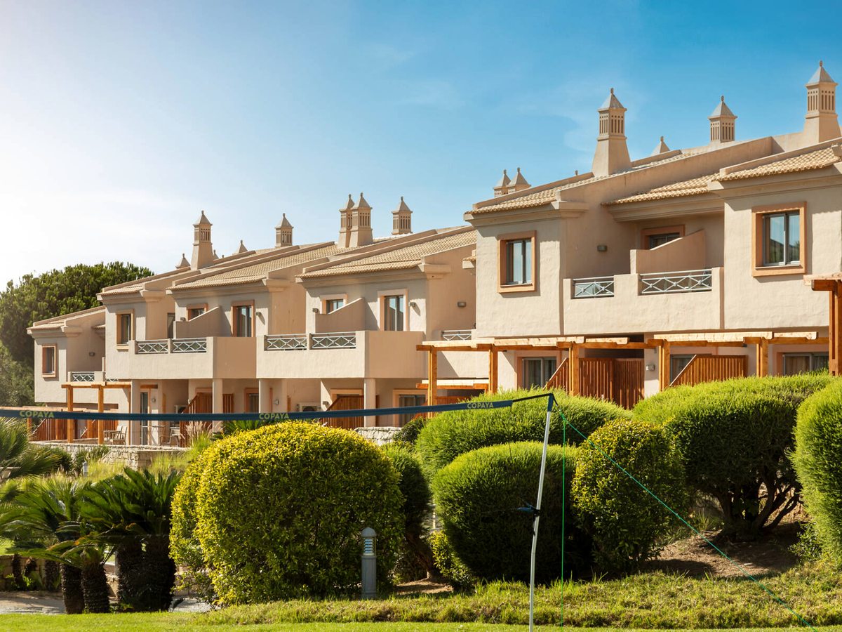 Rows of cream Algarve-style villas with tiled roofs and chimneys, behind clipped topiary and palms in the resort gardens.