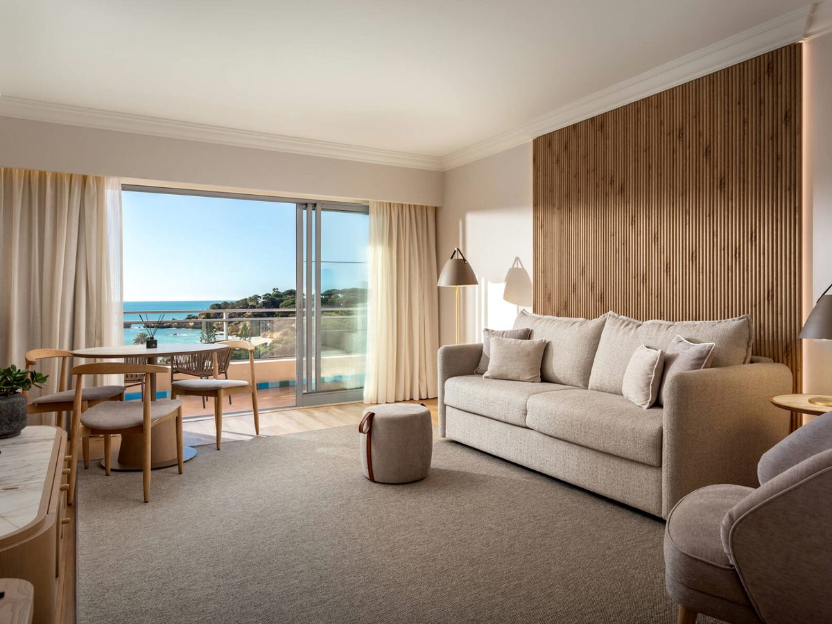 A suite sitting room with a sofa, a small dining table and a balcony looking over the cove.