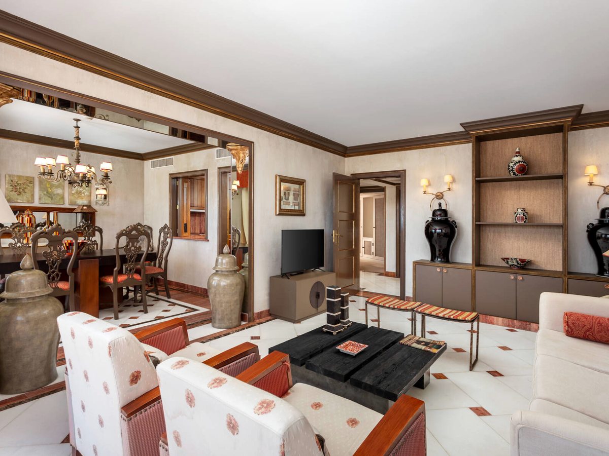 A large formal living room with patterned armchairs and sofas, a separate dining room through an archway and Portuguese ceramics on shelves.
