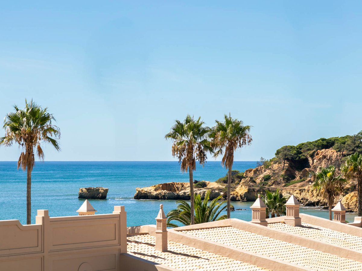 A rocky cove with clear water and palms, seen past a tiled terrace roof.