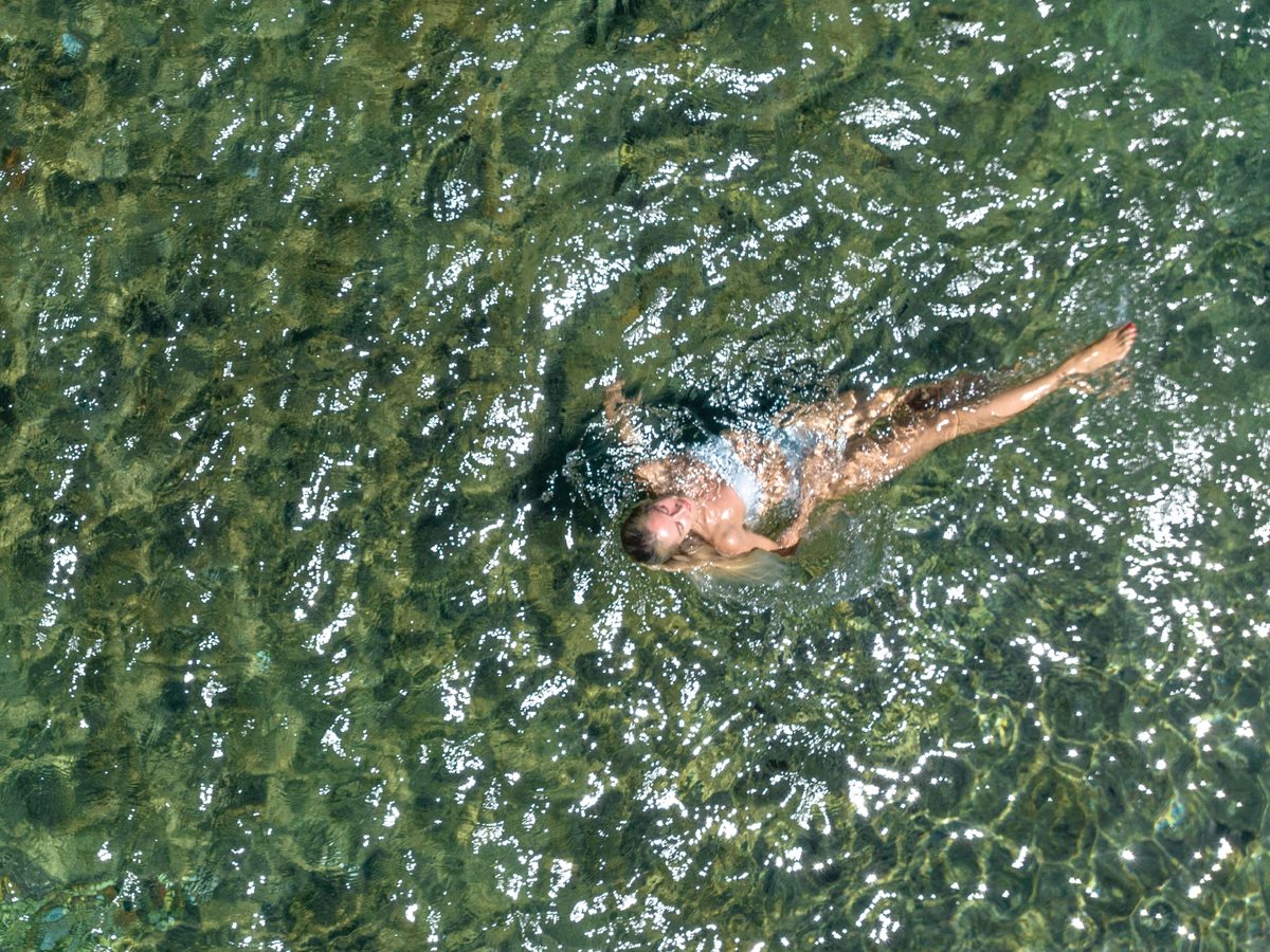An overhead view of a swimmer moving through clear, rippled water.