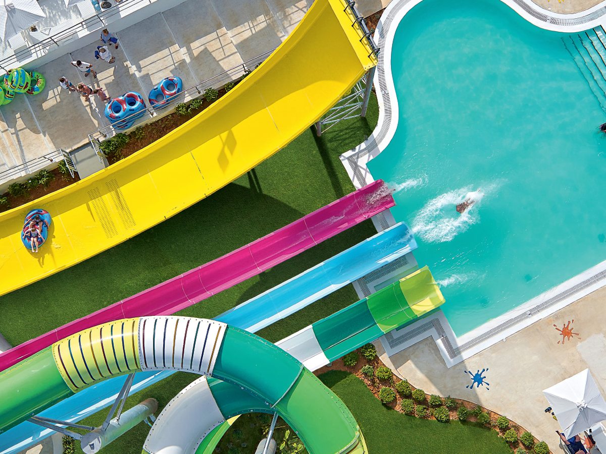 Aerial of tall yellow, pink and green tube water slides curving down into a pool at the aqua park.