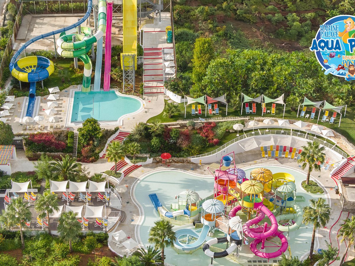 Aerial of the aqua park's children's area with a colourful water-play structure, slides and shallow pools among sun loungers.