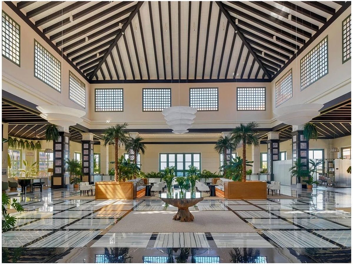 The hotel's double-height lobby, a polished marble floor under a tall timber-beamed roof, with glass-block windows, indoor palms and seating.