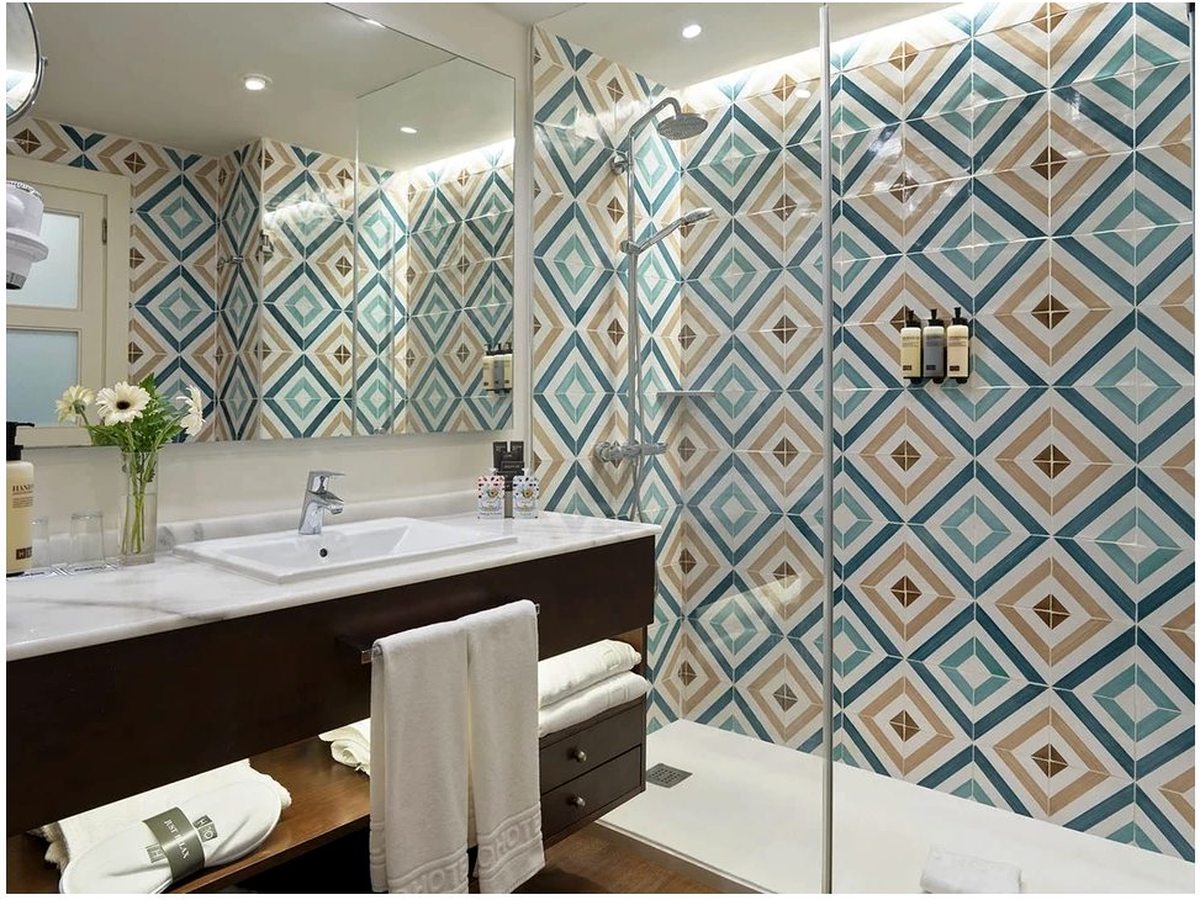 A bathroom with patterned blue and tan wall tiles, a single basin on a marble vanity and a walk-in shower.