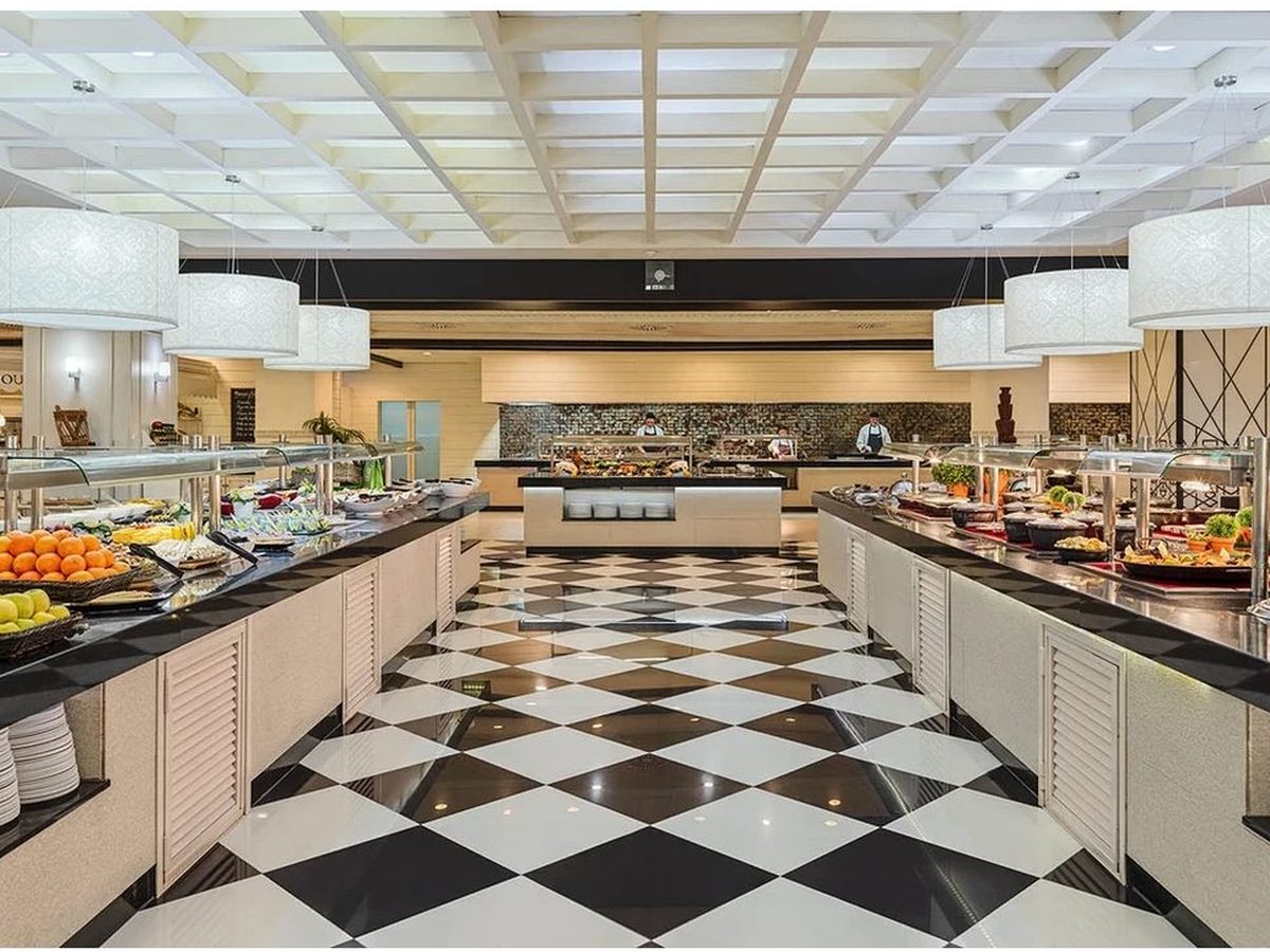 The El Jable buffet restaurant, a long central serving island of dishes on a black-and-white chequerboard floor beneath a bright coffered ceiling.