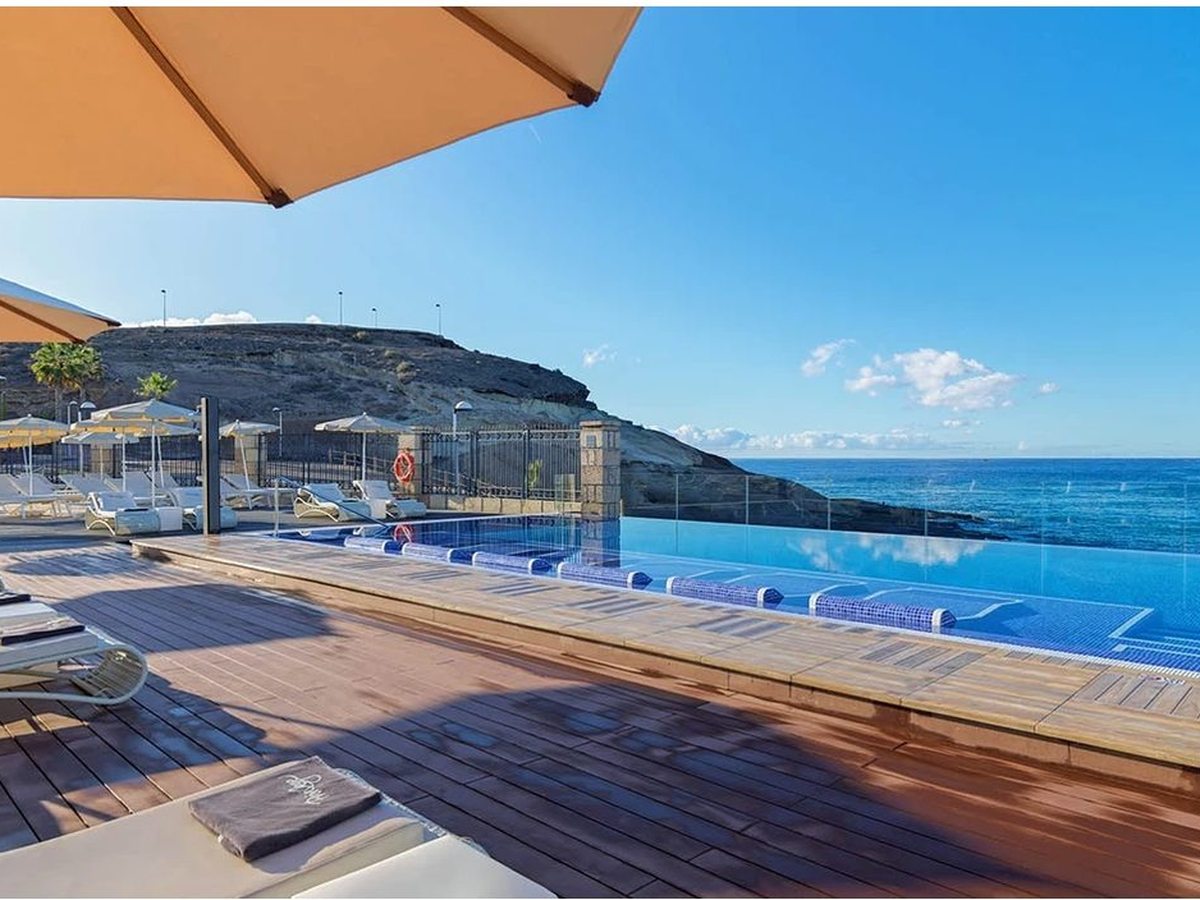 An infinity pool on the seafront, its edge meeting a view of the Atlantic, a parasol and loungers alongside.