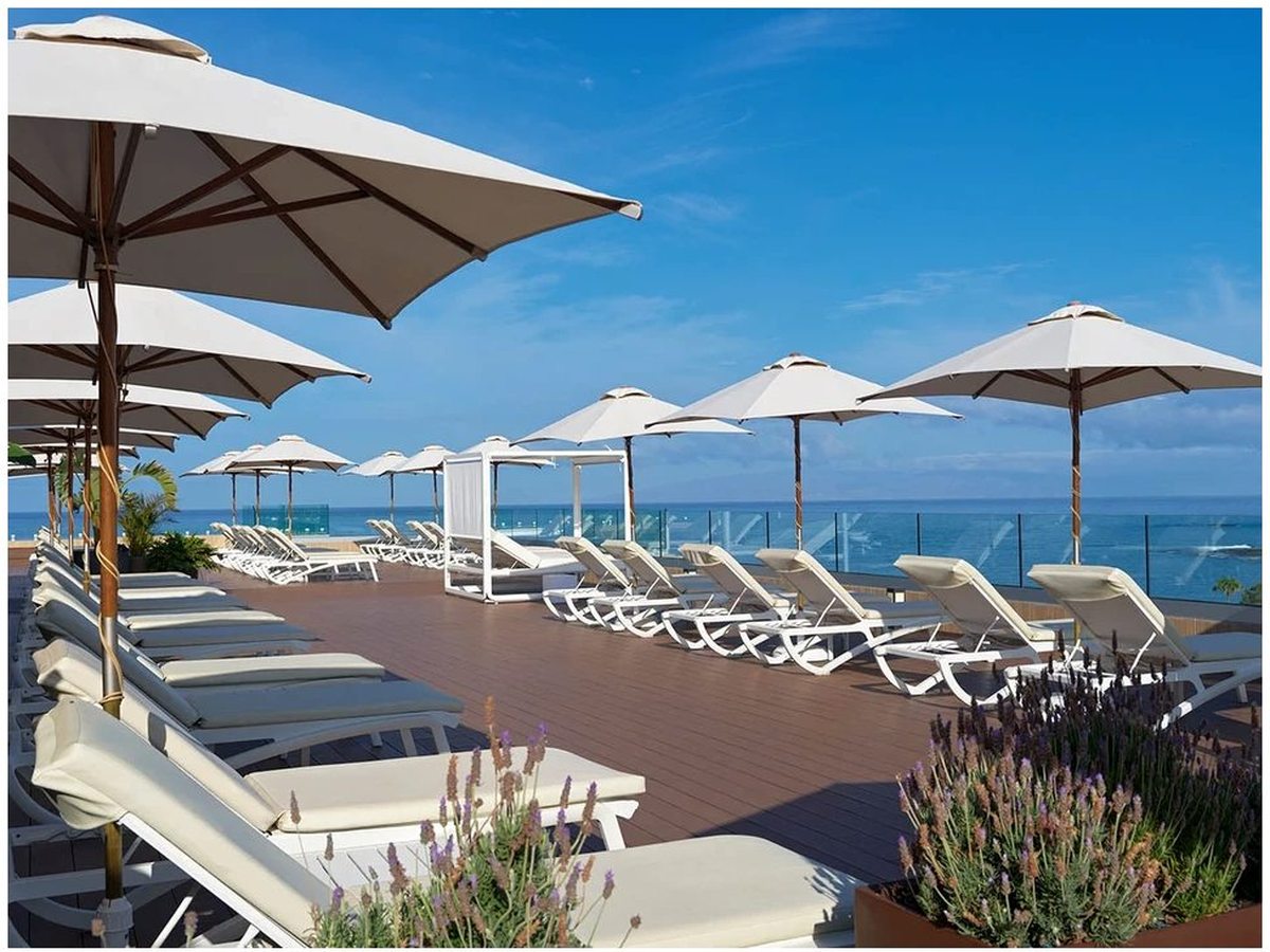 An oceanfront sun terrace lined with white loungers and cream parasols, looking out over the blue Atlantic.